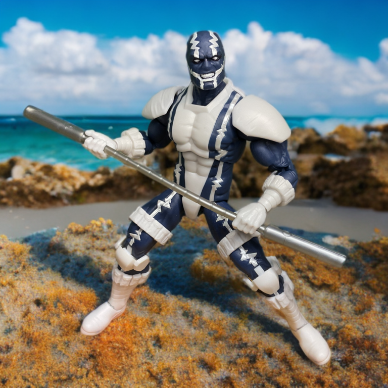 Figura de ação cardíaca em uma pose de batalha agachada segurando um bastão em uma praia rochosa com o oceano ao fundo.