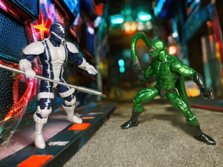 Figura de ação do Cardiac com o bastão levantado, de frente para a figura de ação do Scorpion verde em um beco escuro da cidade.