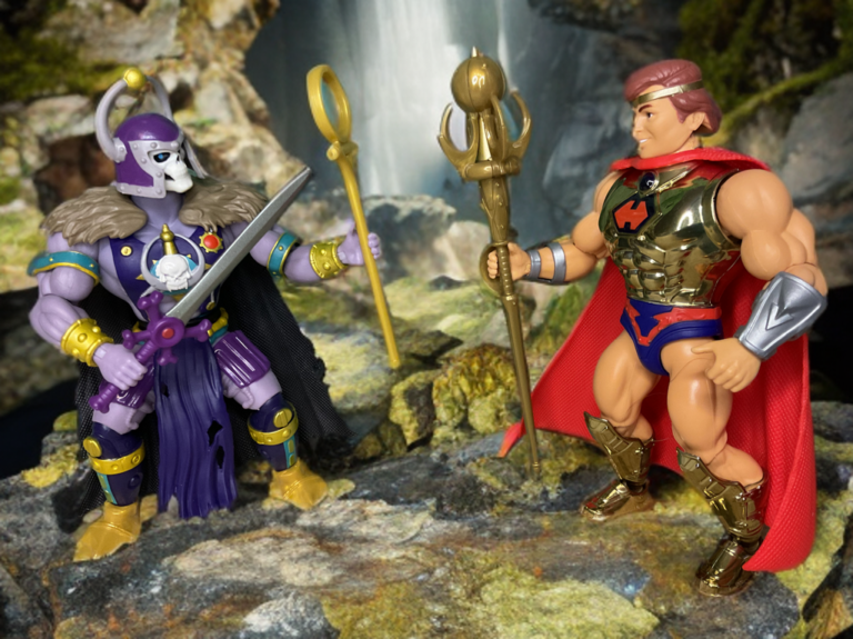 Dynamic battle pose of the Great Black Wizard Origins figure wielding sword and Shaping Staff with flowing cape as he encounters He-Ro.