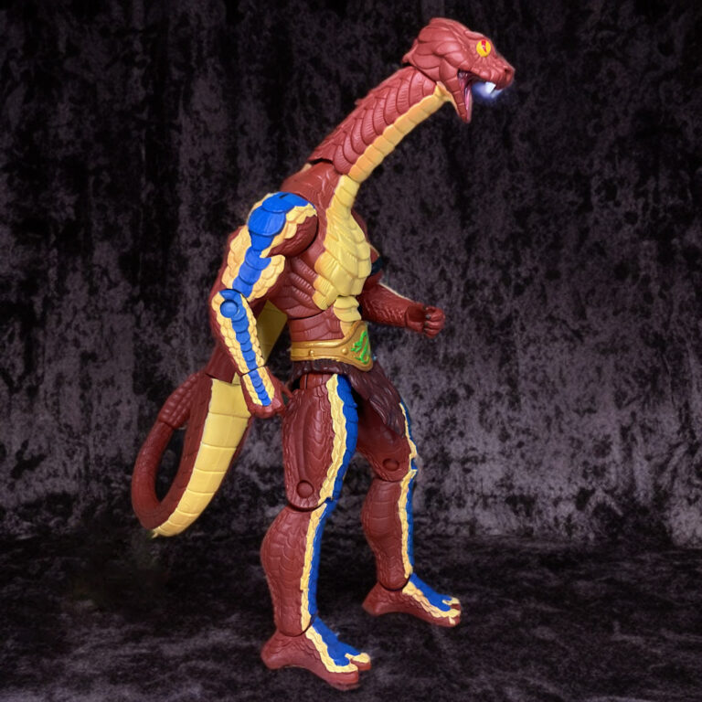 MOTU Classics Rattlor Figur inmitten alter Ruinen, rote Schuppen, gelber Klapperschwanz und verlängerter Hals in Angriffshaltung.