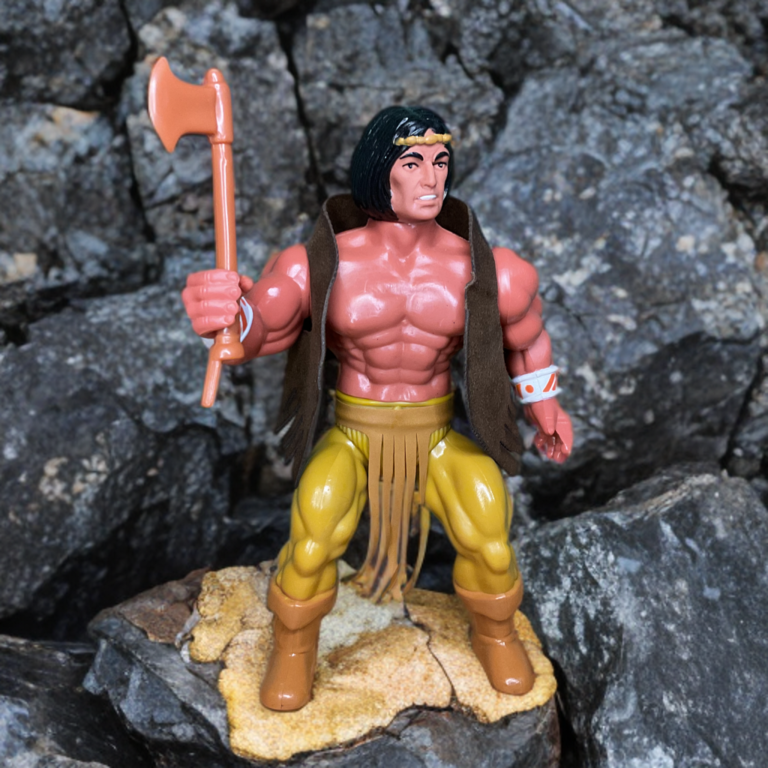 : 1982 Remco Arak Son of Thunder action figure debout sur une falaise rocheuse accidentée avec un paysage lointain, hache à la main, cheveux roux balayés par le vent, jouet vintage dans un décor de montagne naturel.