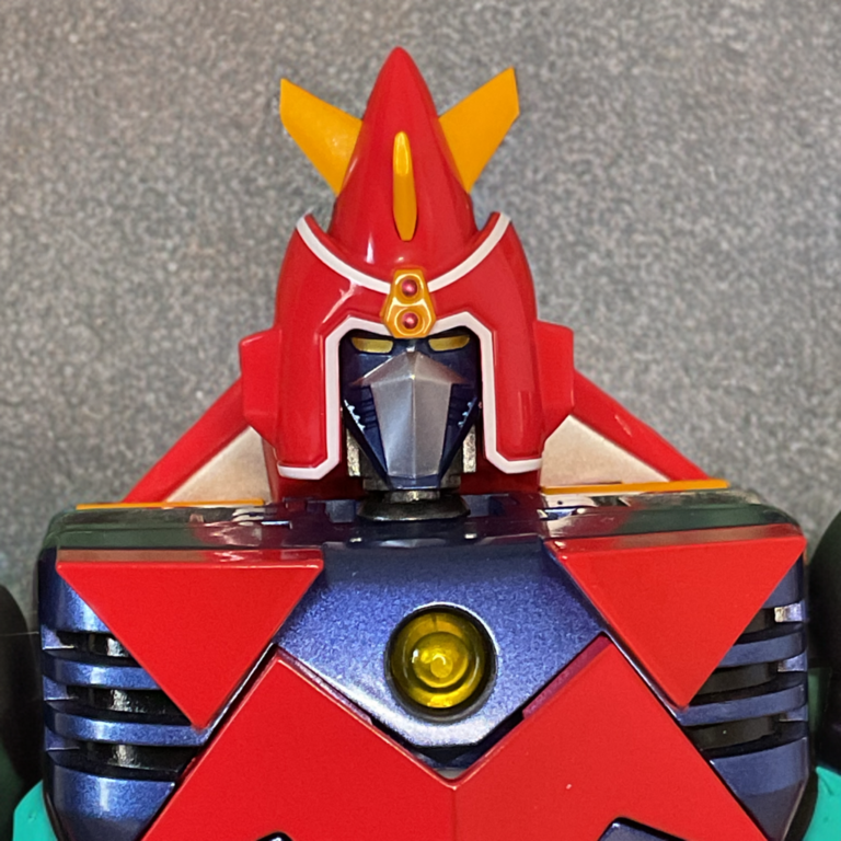 Detailed macro shot of Voltes V GX-31SP combined head unit with translucent red visor and chrome chest emblem, sharp sculpting and tampo printing visible.