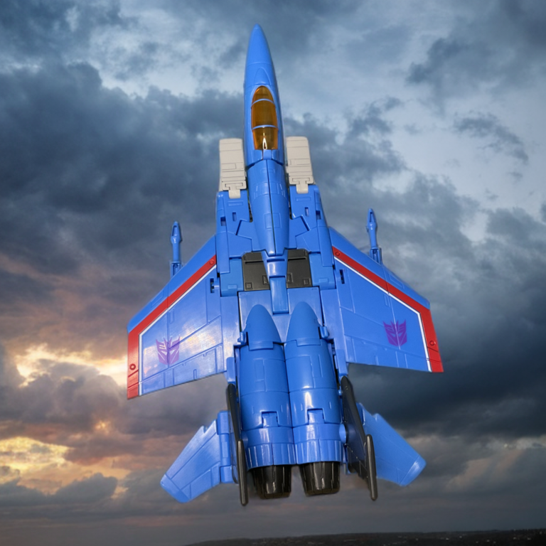 スタジオシリーズ サンダークラッカーのジェットモード、青いディセプティコンの戦闘機が空を背景に飛んでいる。.