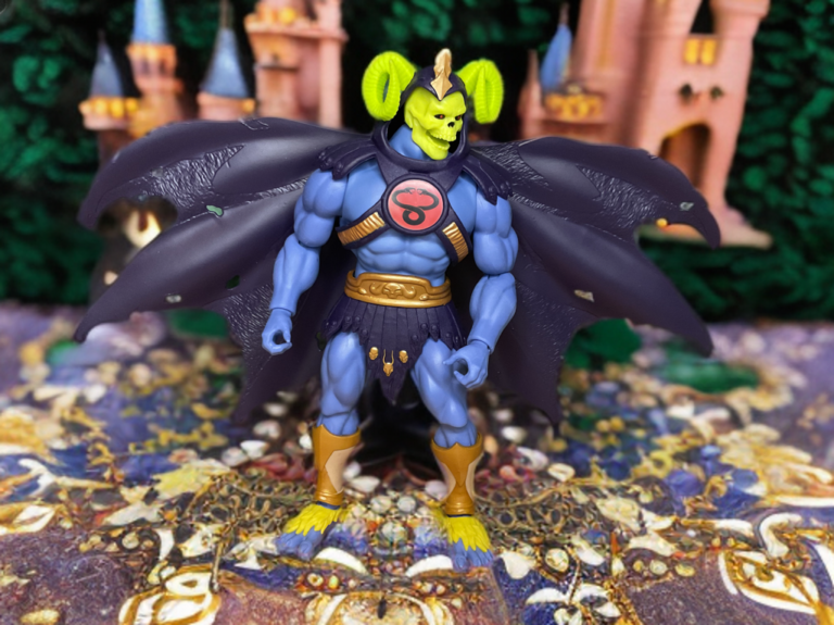 Front view of Skell-Ra MOTU Origins figure in Skell-Ra mode, blue torso with harness and flowing purple cape.