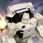 Transformers Earthrise Deluxe Runamuck figure posed in robot mode on a neutral background, highlighting detailed head sculpt, Decepticon insignia, and premium white plastic with gold accents.