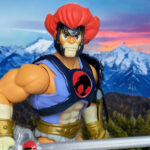 Masters of the Universe Origins Lion-O action figure standing heroically in a golden sunset field, Sword of Omens, red mane flowing, hybrid Thundercats MOTU style.
