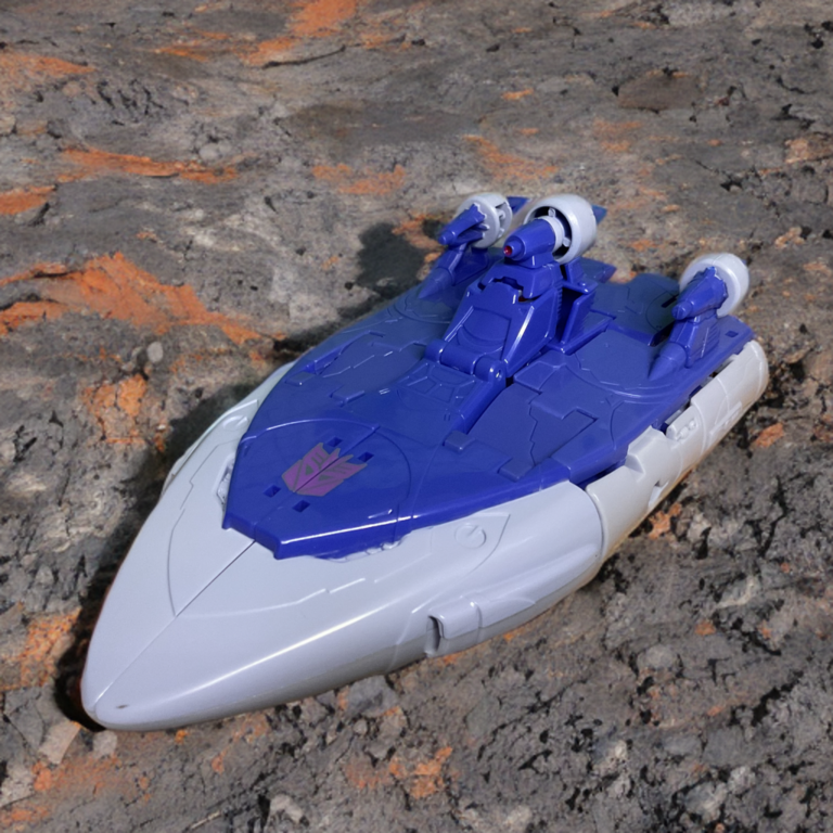 Blue and white Studio Series Scourge in hovercraft vehicle mode, front view with thrusters and pointed nose visible.