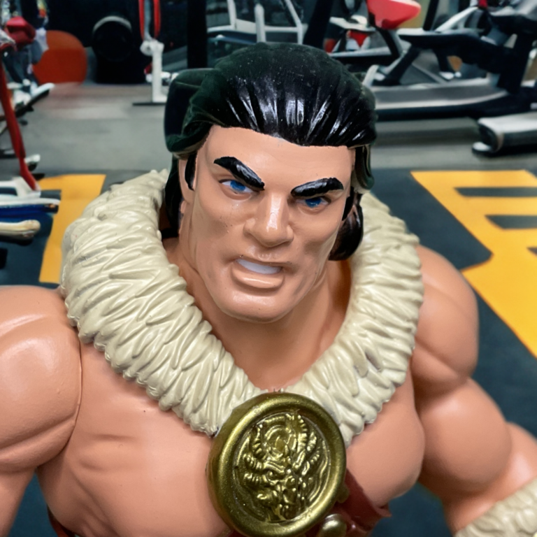 Nahaufnahme des Gesichts der Legends of Dragonore Barbaro-Actionfigur im Fitnessstudio. Man sieht die ständigen missbilligenden Augenbrauen, die gerunzelte Stirn und den gemeißelten Kiefer, der während eines schweren Hebevorgangs in High-Definition-Stress versetzt ist.