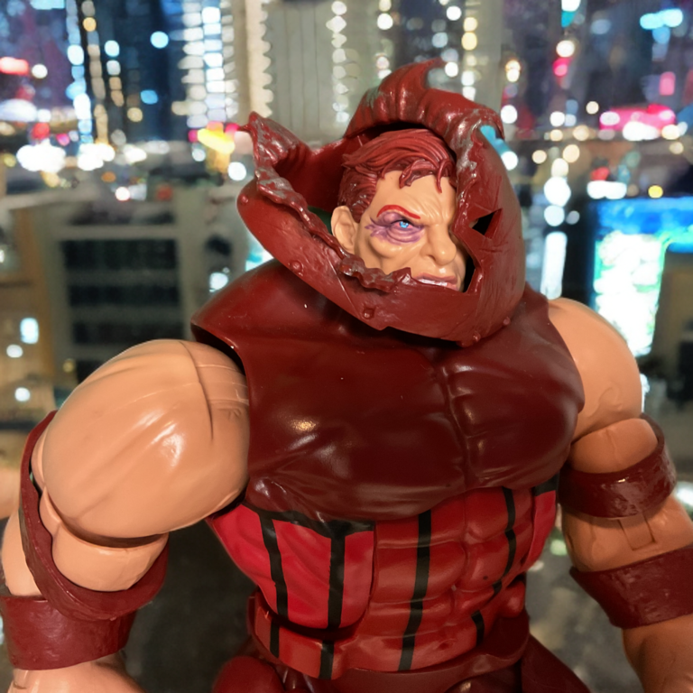 Close-up of Juggernaut's busted helmet, bruised face and massive build, mystical power glowing.