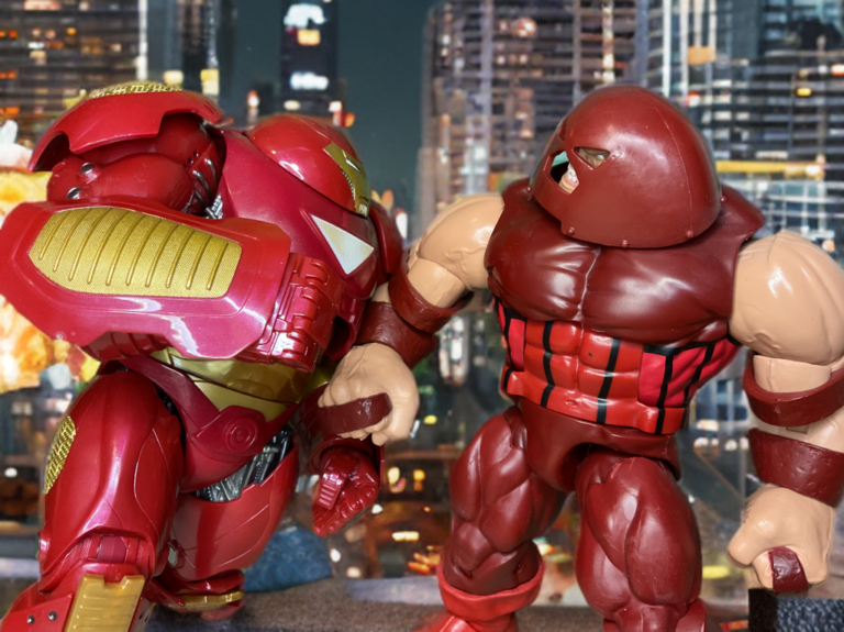 Juggernaut driving Hulkbuster backward through debris, momentum unstoppable in a relentless assault.