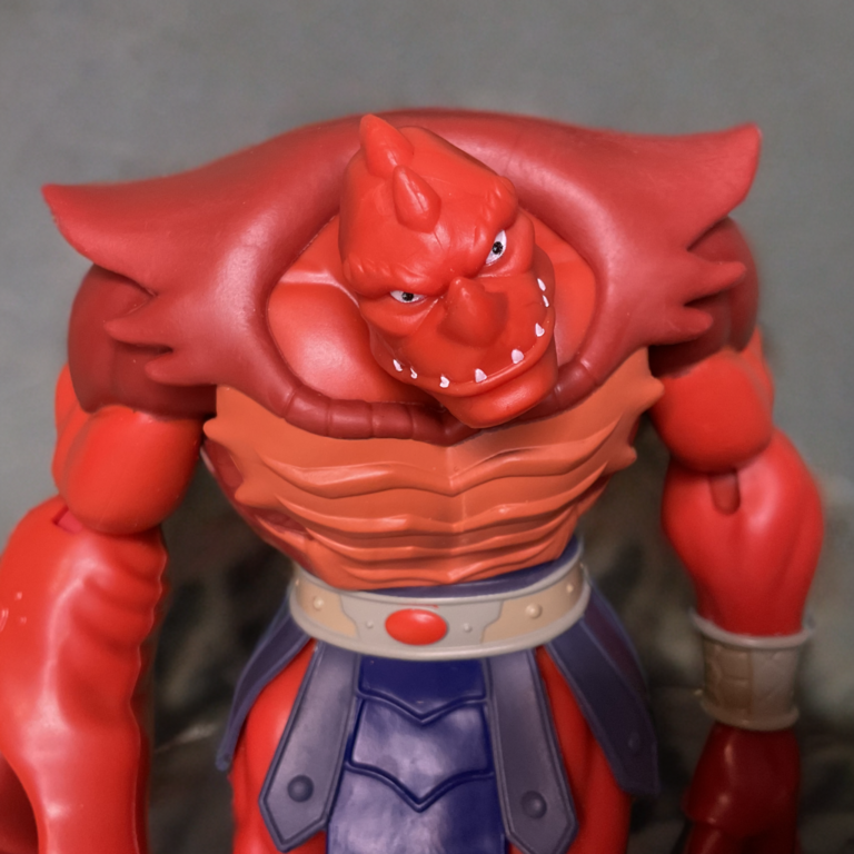 Gros plan sur la sculpture chitineuse du torse et le pagne bleu de la figurine Origins Clawful.
