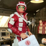 High-resolution hero shot of the 6-inch G.I. Joe Classified Series #186 Lifeline action figure in full pose, showcasing his bright red uniform, medical gear, and heroic stance against a dynamic barrack backdrop.