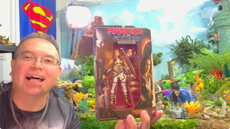 YouTube reviewer Super Dave smiling while holding up a boxed Masters of the Universe Chronicles Teela action figure in his review studio.